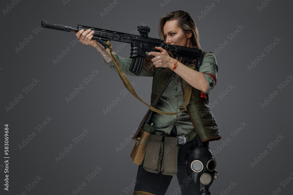 Portrait of military woman with rifle looking to side isolated on grey background.