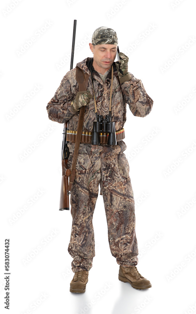 Full-length portrait of duck hunter with a rifle on his shoulder isolated on white background. Fifty-year-old man in hunting uniform calling by mobile phone and posing in studio. Full-length portrait of duck hunter with a rifle on his shoulder isolated on white background. Fifty-year-old man in hunting uniform calling by mobile phone and posing in studio.