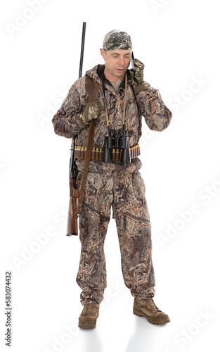 Full-length portrait of duck hunter with a rifle on his shoulder isolated on white background. Fifty-year-old man in hunting uniform calling by mobile phone and posing in studio.