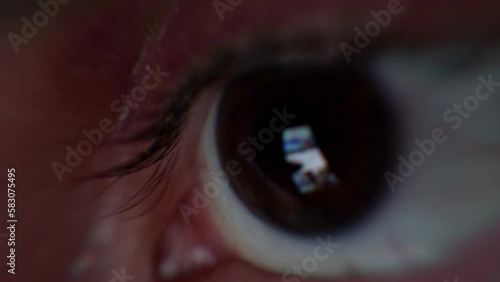 Scrolling smartphone feed with tech news. Man's eye watching smartphone screen while scrolling through online news and information. Online information and fake news, closeup macro detail of an eye.