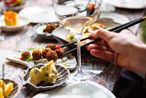 hand eating food in restaurant. wine, cheese, meat, vegetables and other appetizers on table