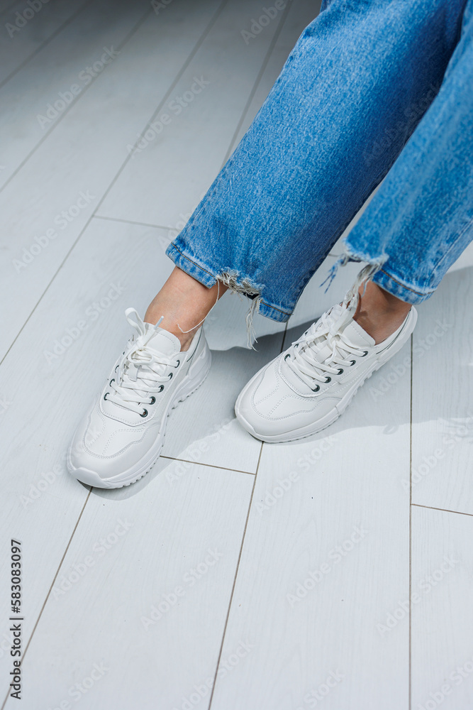 Female legs in white stylish sneakers. Casual women's fashion. Comfortable shoes for women. Women's comfortable summer shoes. Female legs in white stylish sneakers. Casual women's fashion. Comfortable shoes for women. Women's comfortable summer shoes.