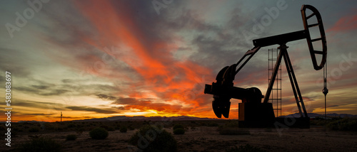 Silhouette of oil pump in desert landscape at sunset. Space for text and or images.