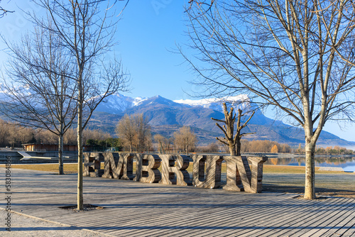A scenics view of the Embrun, France lake with wooden sign, snowy mountains range in the background under a majestic blue sky