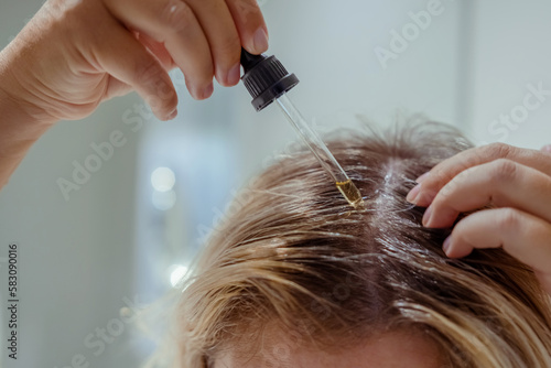  Woman applies oil to her hair with pipette. Beauty caring for scalp and hair. 