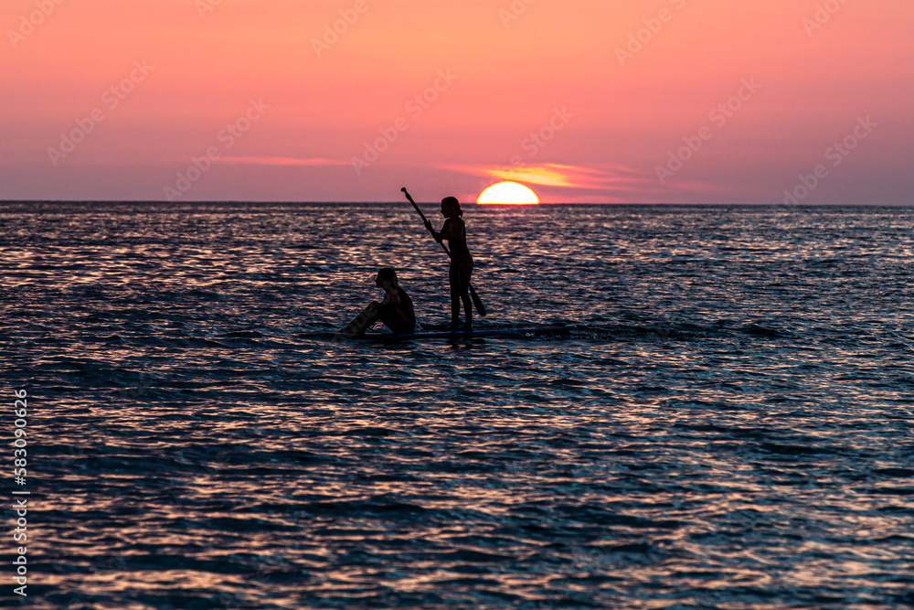 silhouette of  two girls paddling in the sunset