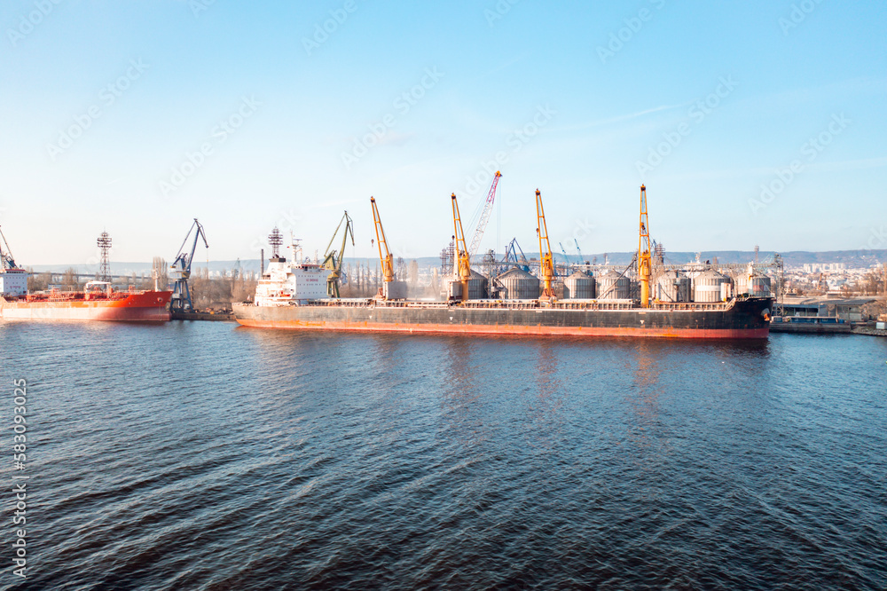 Aerial drone shot grain deal 2023. Bunkering of dry cargo ship with grain at sunset golden hour. Loading grain on sea dry cargo vessel with harbor crane