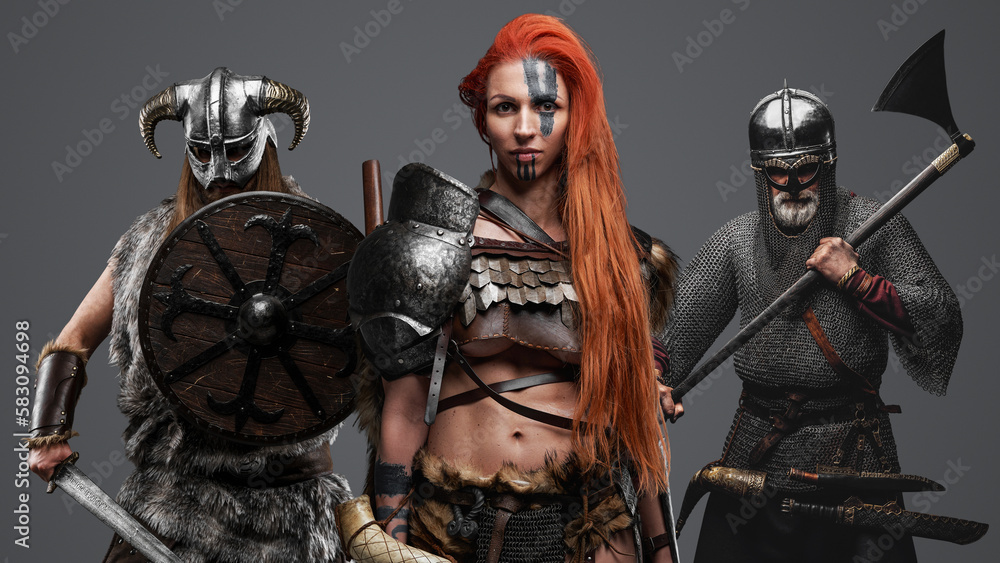 Studio shot of barbaric viking woman with redhairs and two warriors on her sides.
