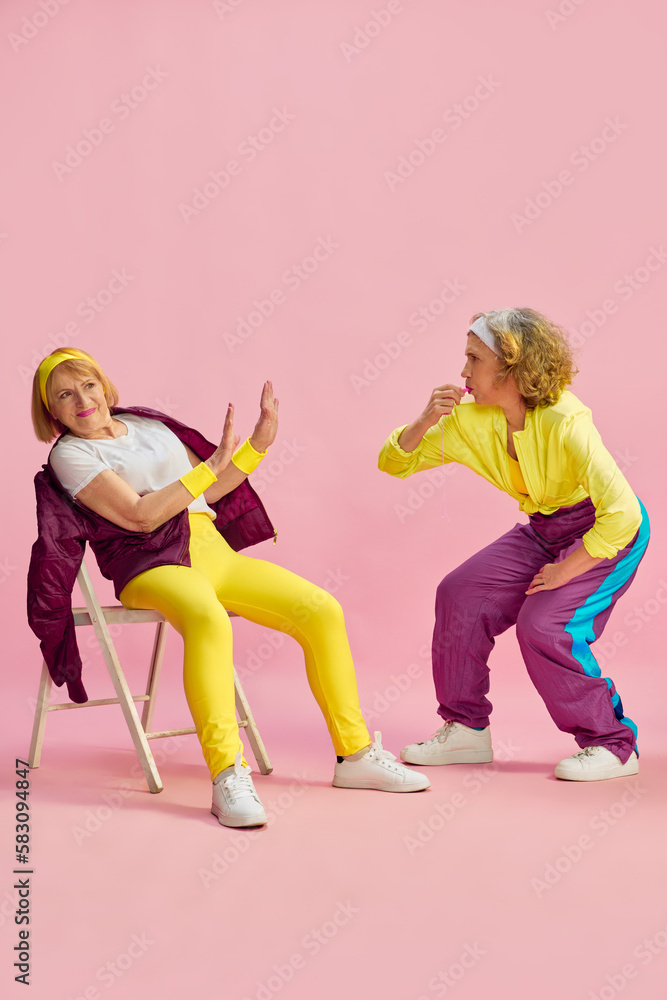 Naklejka premium Competition. Two elderly sportive women in colorful uniform training, posing against pink studio background. Concept of sportive lifestyle, retirement, health care, wellness. Ad