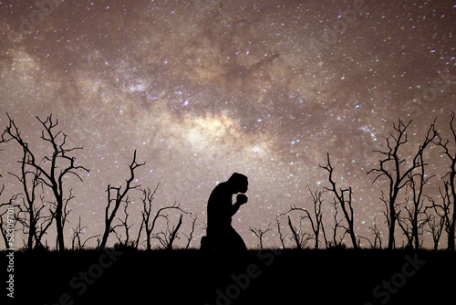 Man silhouette kneeling praying to god hopefully with the beautiful Milky Way