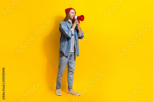 Full length photo of positive funny man wear denim screaming bullhorn emtpy space isolated yellow color background