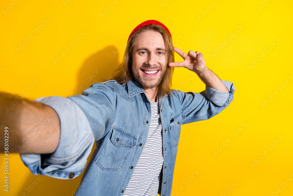 Naklejka premium Photo of funky perky positive guy long hairdo dressed jeans shirt making selfie showing v-sign isolated on yellow color background