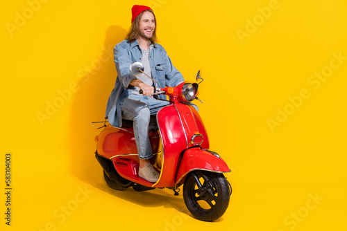 Full length photo of sweet positive man wear denim jacket riding moped looking emtpy space isolated yellow color background