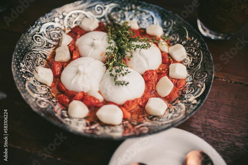 The board is set up on a long buffet table. The cheeses are arranged alongside sliced cured meats, fresh grapes, and berries, and the warm glow of the overhead lights adds to the overall ambiance 
