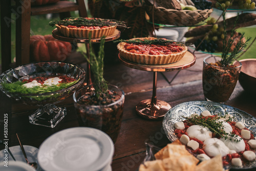 The board is set up on a long buffet table. The cheeses are arranged alongside sliced cured meats, fresh grapes, and berries, and the warm glow of the overhead lights adds to the overall ambiance 