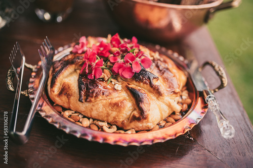 The board is set up on a long buffet table. The cheeses are arranged alongside sliced cured meats, fresh grapes, and berries, and the warm glow of the overhead lights adds to the overall ambiance 