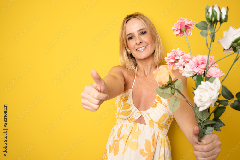 Portrait of a smiling playful cute woman holding flowers isolated on a yellow background