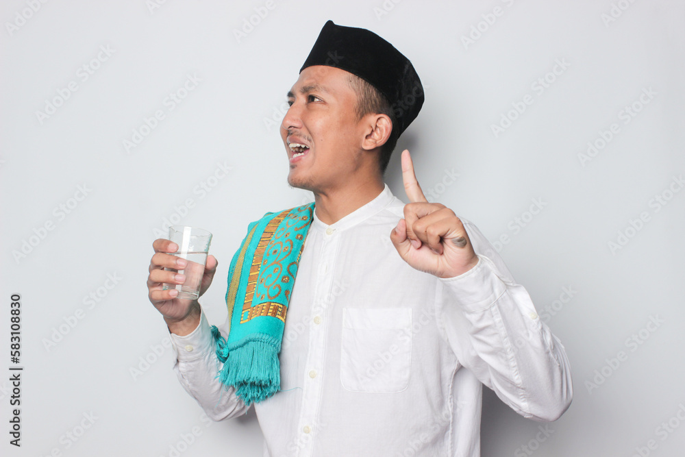 Happy asian muslim man standing while drinking a glass of water. Healthy concept in ramadan. Isolated on white Happy asian muslim man standing while drinking a glass of water. Healthy concept in ramadan. Isolated on white