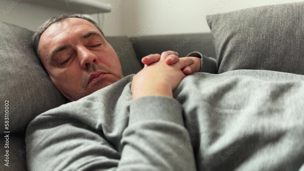 A middle-aged man sleeps on the couch wearing wireless headphones. Tired and a man will take a nap after a hard day's work, rest on the weekend A middle-aged man sleeps on the couch wearing wireless headphones. Tired and a man will take a nap after a hard day's work, rest on the weekend