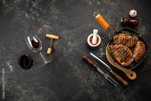 Marbled beef steaks in a grill pan with wine glass on a dark background. Restaurant menu, dieting, cookbook recipe top view