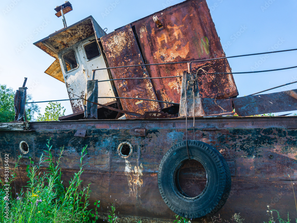 Old rusty ships lie on the riverbank. The river bank and rusting ships. Pier with old ships on the shore. Old tugs are rusting on the riverbank.