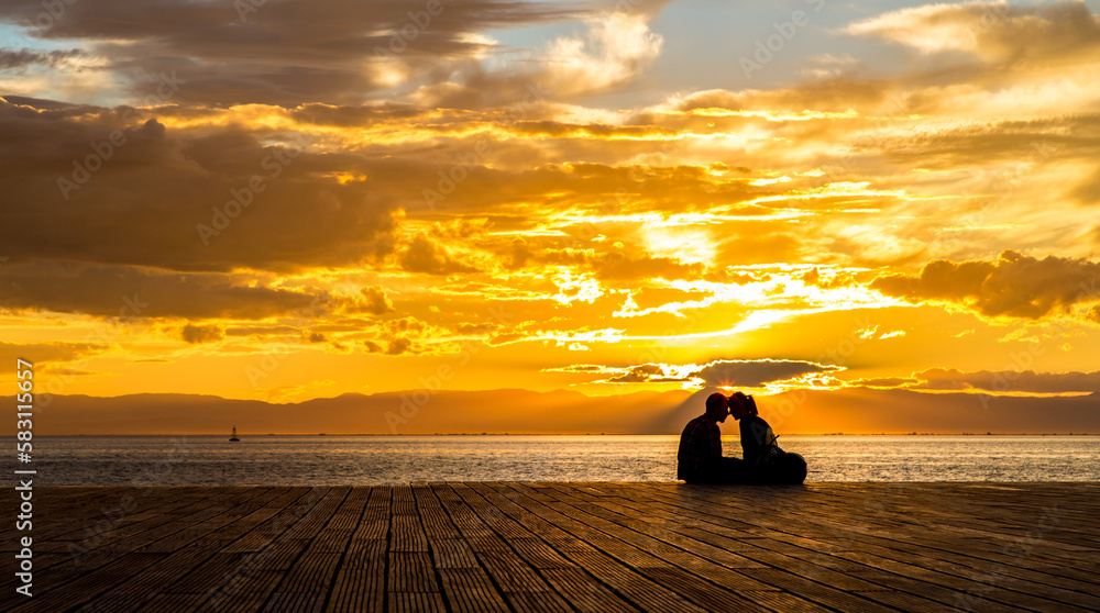 silhouette of a couple in love, sitting on a pier in sunset