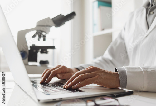 Scientist or student using laptop computer and microscope photo