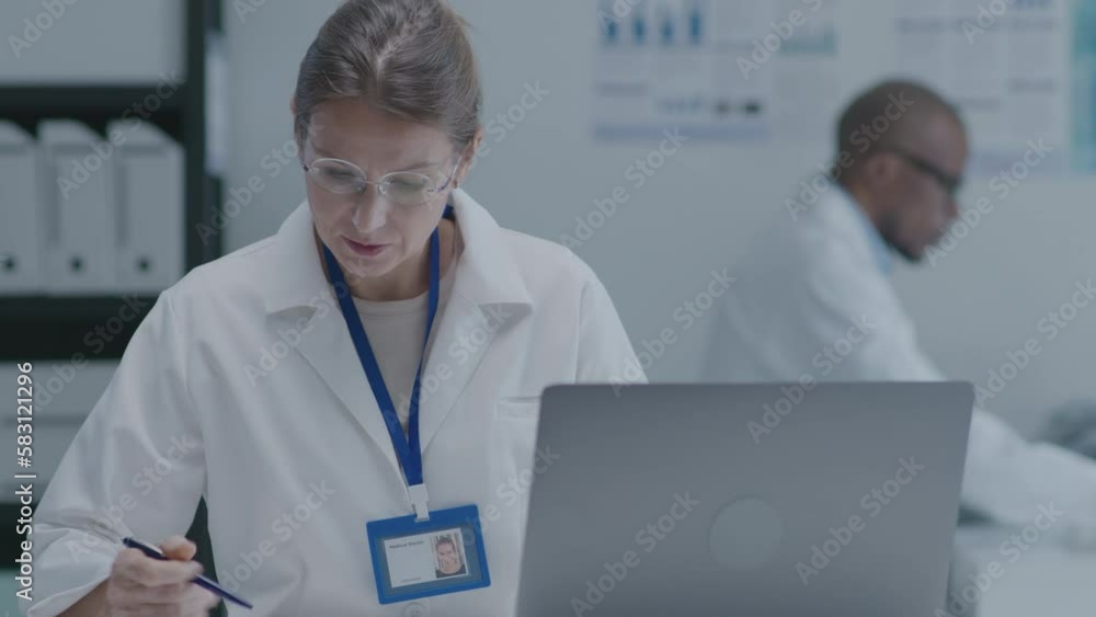 Female doctor sitting at desk, working with laptop, making notes in the clinic. Medium shot Female doctor sitting at desk, working with laptop, making notes in the clinic. Medium shot
