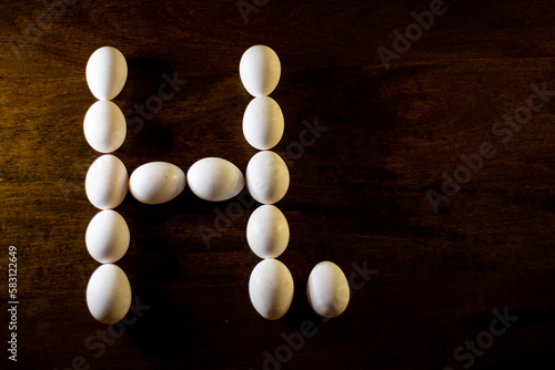 white chicken eggs forming the letter H with a stop on a wooden background