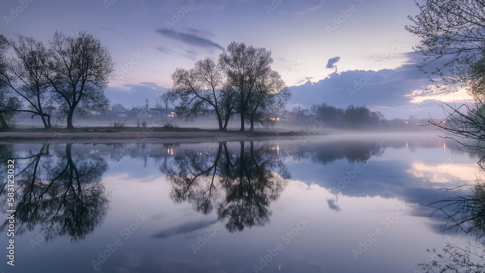Fototapeta premium Impressively beautiful fabulous morning on the river at blue hour. The rising sky is reflected in the river during a foggy morning. Panoramic view of the beautiful mystical lake.