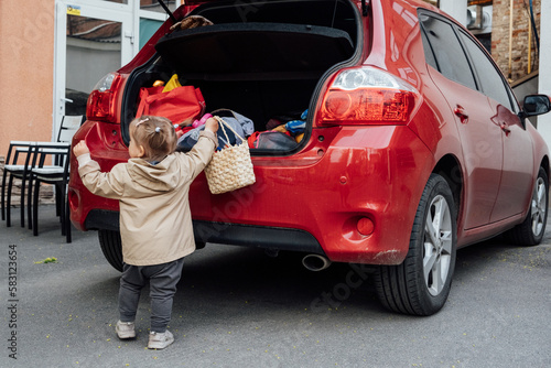 Fototapeta Naklejka Na Ścianę i Meble -  Family road trip where toddler little girl is helping to load up the trunk with suitcases and backpacks. Little girl help and put bags into the car trunk