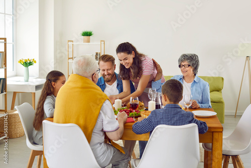 Multi generation family celebrating Thanksgiving at home. Gathered together at table  family of young people and elderly people eat  drink  serve food  joke and have fun. Concept of family celebration
