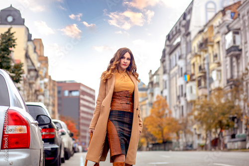 Modern brunette girl in a brown coat and high boots walking in the city on the road. Walk. Autumn. Fashion concept