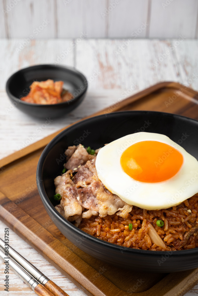 Closeup of Kimchi rice with grilled brisket sliced and fried egg in black bowl on wooden table. Closeup of Kimchi rice with grilled brisket sliced and fried egg in black bowl on wooden table.