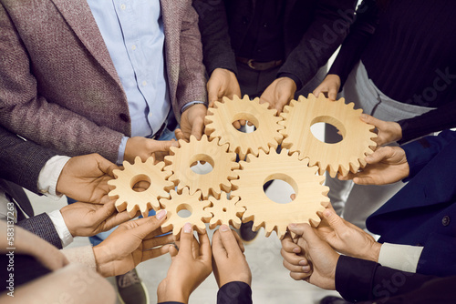 Team work, unity, partnership or integration. People at business training learn to interact and solve business issues using cogwheels. Close up of wooden gears of different sizes in hands of people.