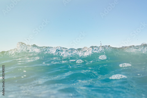 Carefree ocean waves. Blue water surface with small waves. Background on the theme of holidays and vacations at sea with the family. Water with white foam in soft focus on a bright sunny day.