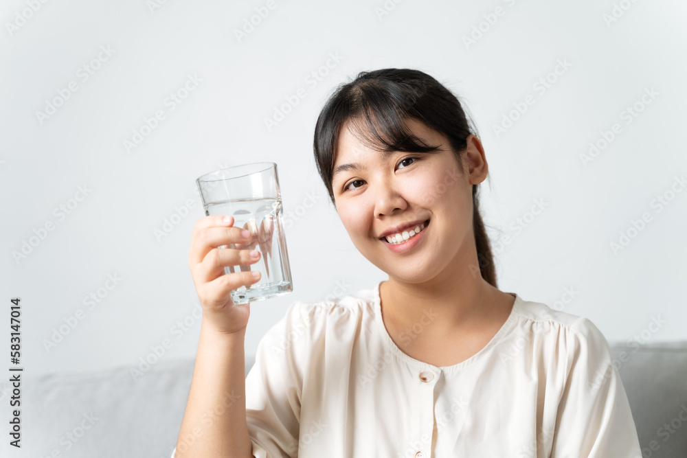 healthy beautiful young woman holding a glass of water sitting on the couch at the livingroom. healthy beautiful young woman holding a glass of water sitting on the couch at the livingroom.
