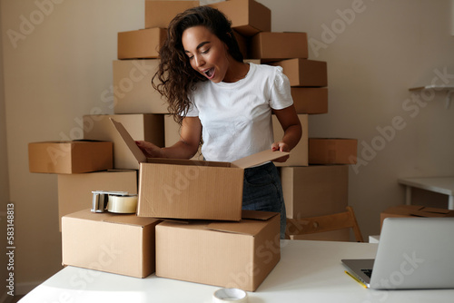 Online store owners use a laptop to prepare parcels of clothing for shipping. Cheerful woman working in the office. Entrepreneur woman doing small e-commerce business © Alexandr