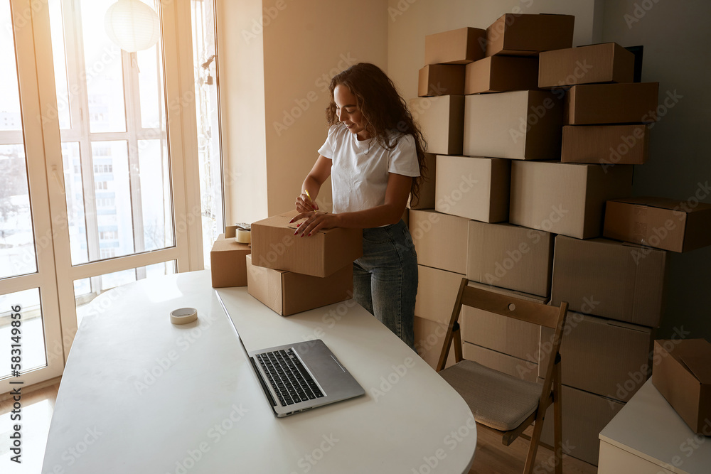 Online store owners use a laptop to prepare parcels of clothing for shipping. Cheerful woman working in the office. Entrepreneur woman doing small e-commerce business Online store owners use a laptop to prepare parcels of clothing for shipping. Cheerful woman working in the office. Entrepreneur woman doing small e-commerce business