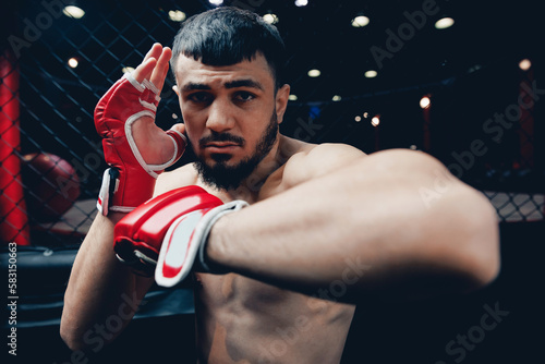 Portrait MMA fighter with red boxing gloves trains in gym, cage octagon dark background © Parilov