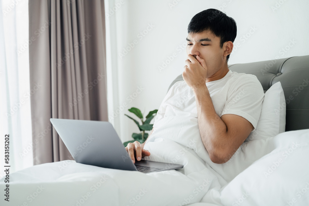 Sleepy man yawning on bed using laptop computer. Sleepy man yawning on bed using laptop computer.