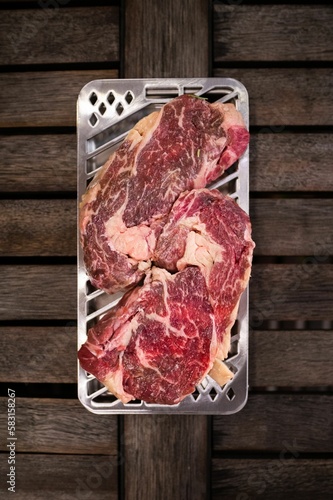 Vertical top view of a silver metal platter with raw steak slices on a woodne table photo