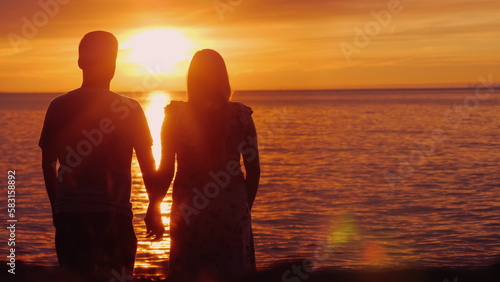 Romantic multi-ethnic couple admires the scenic sunset over the sea. Holding hands, rear view. Harmony in relationship concept © StockMediaProduction