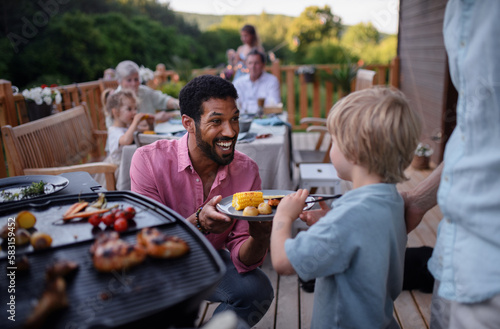 Father grilling meat and vegetable on grill during family summer garden party.