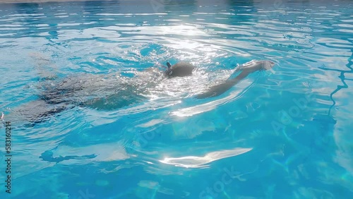 Busninessman male swimmer swimming breaststroke style in luxury pool wearing goggles and backlit by sun, slow motion