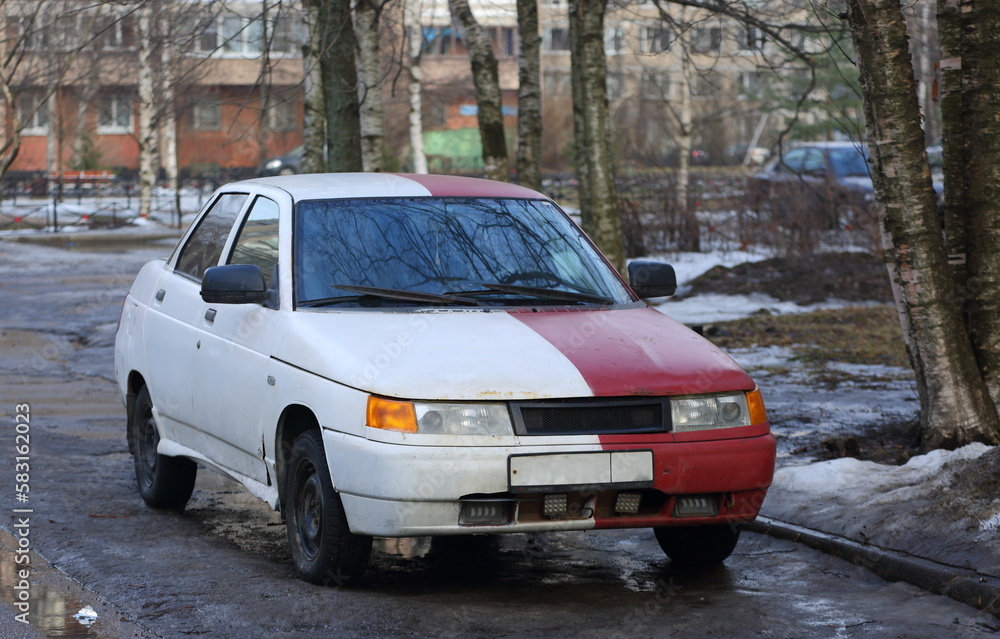 An old red and white car is parked on the city street, Podvoysky Street, St. Petersburg, Russia, March 2023