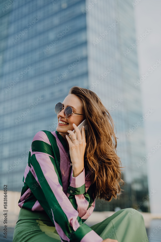 Portrait of beautiful young woman with smartphone outdoor in city, during sunset.
