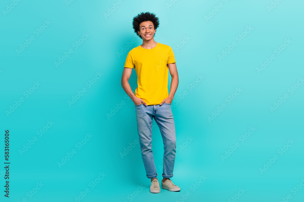 Full length photo placard of young positive guy wear yellow t-shirt denim jeans hands pockets model brand clothes isolated on cyan color background Full length photo placard of young positive guy wear yellow t-shirt denim jeans hands pockets model brand clothes isolated on cyan color background