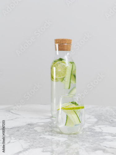 Bottle with one glass of beauty water lemonade made of cucumber and lime standing on the white marble table 