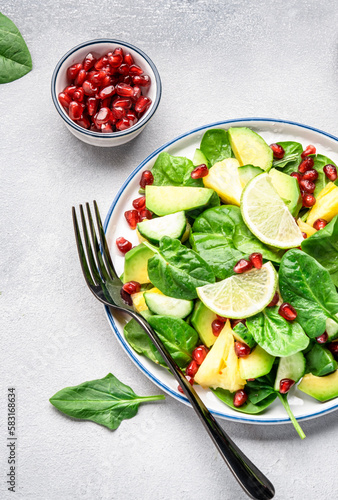 Fresh vegan salad with pineapple, spinach, avocado and pomegranate seeds, gray kitchen table, top view. Healthy eating, clean food, diet, weight loss concept